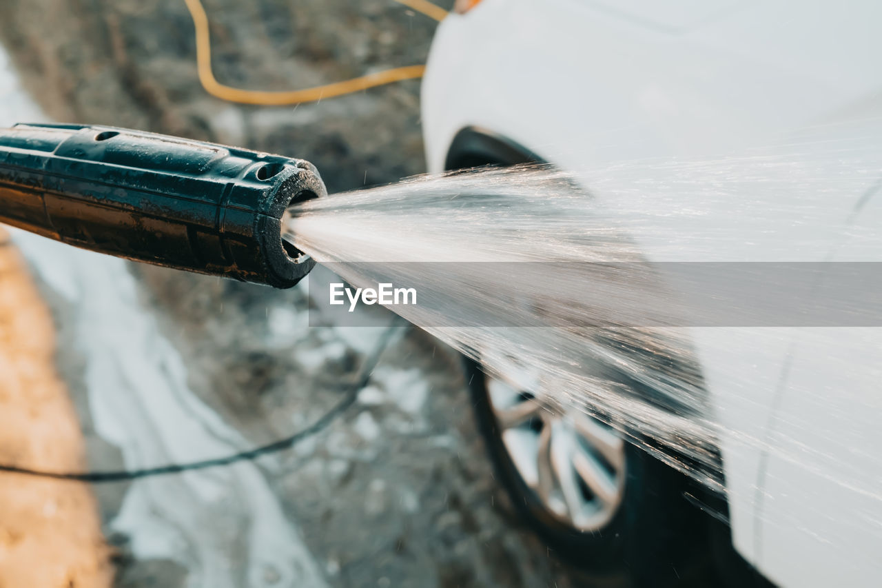 Manual car wash with jet of high pressure water. worker washes white automobile outside 