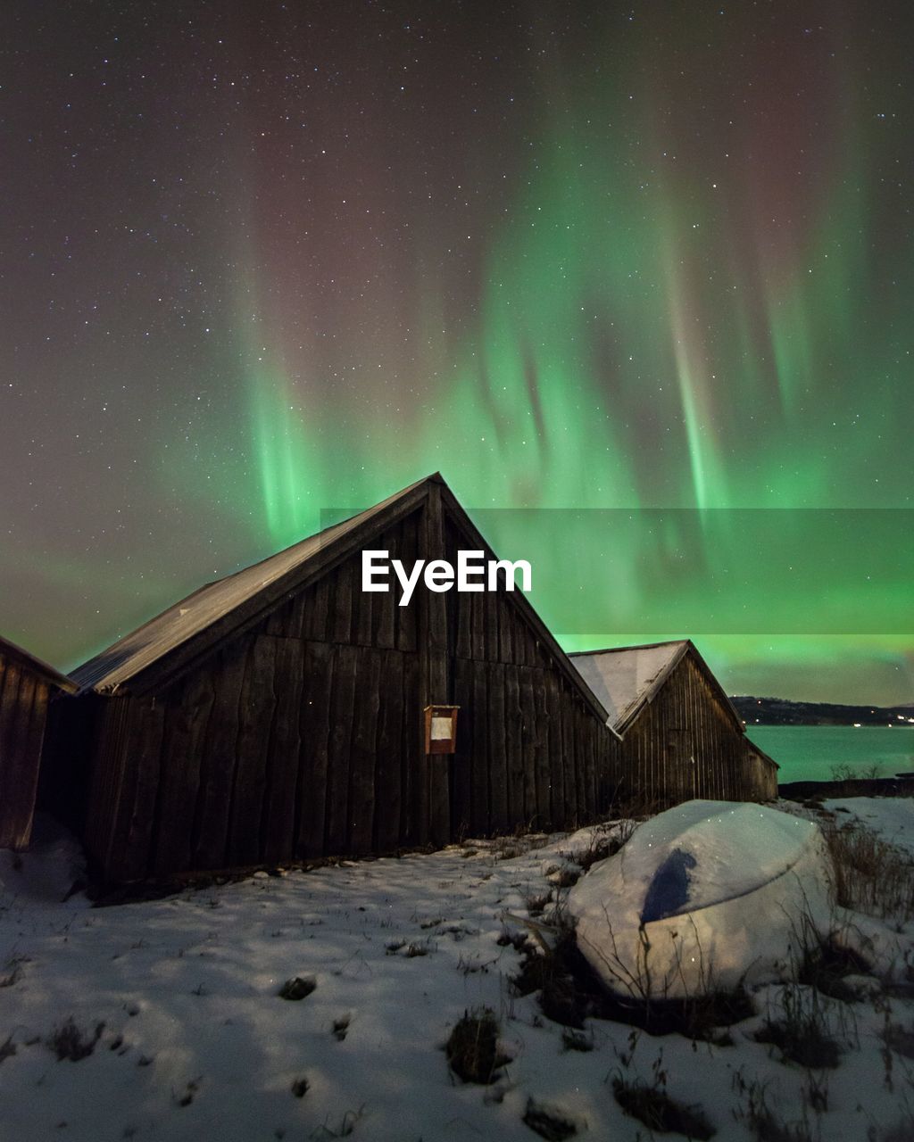 Wooden houses by snowcapped field against aurora borealis in sky