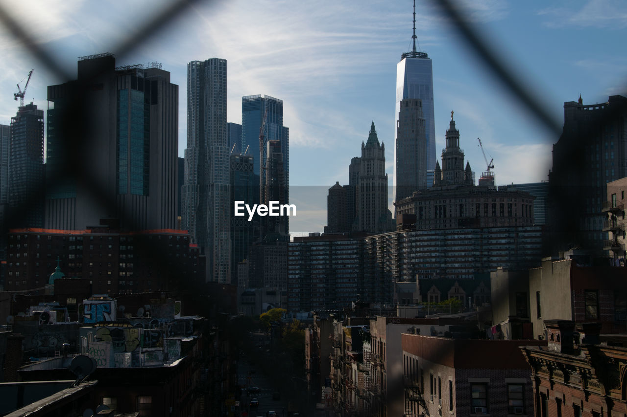 Buildings in city seen through chain link fence