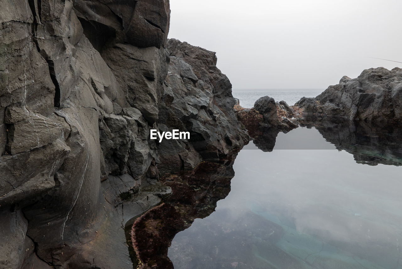 rock, water, nature, terrain, beauty in nature, cliff, rock formation, sky, scenics - nature, land, sea, tranquility, coast, environment, geology, no people, beach, outdoors, landscape, mountain, non-urban scene, travel destinations, day, tranquil scene, travel, formation, reflection