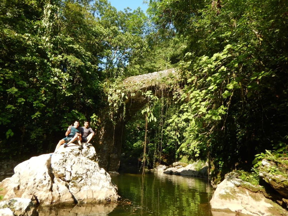 WOMAN SITTING ON ROCK IN RIVER AMIDST TREES IN FOREST