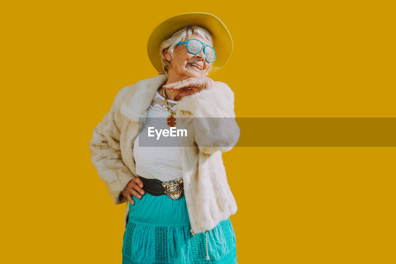 Smiling woman standing against yellow background