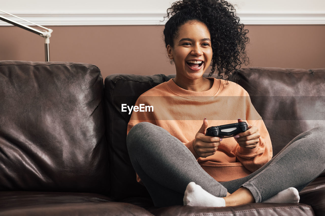 Smiling young woman playing video game sitting on sofa