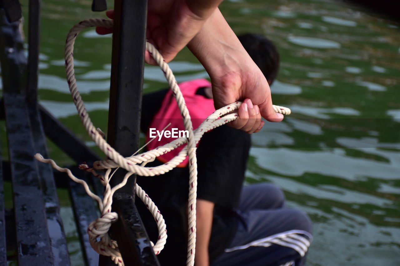 Cropped hands of person tying rope on metal