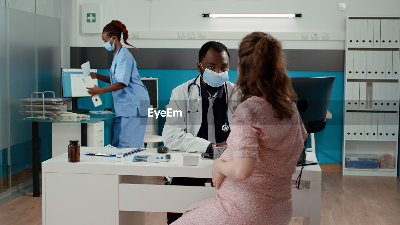 Doctor wearing mask examining pregnant woman at clinic