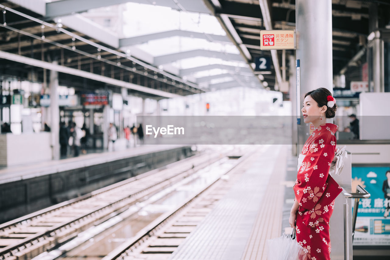 Side view of woman with umbrella standing at railroad station