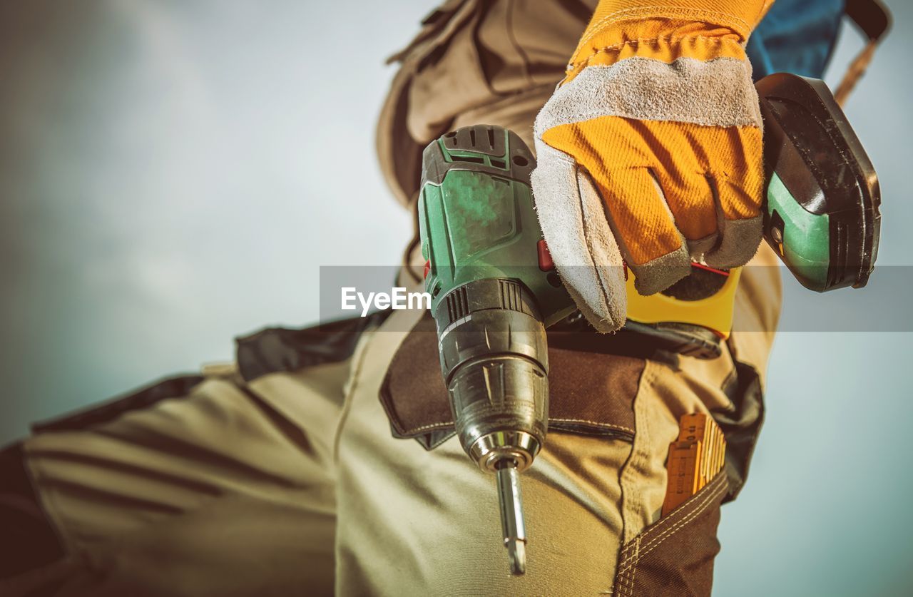 Midsection of manual worker holding drill