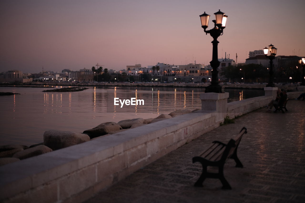 ILLUMINATED STREET LIGHT BY RIVER AGAINST SKY AT NIGHT