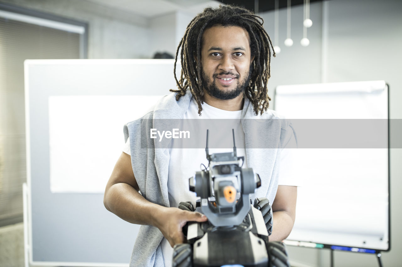 Smiling technician holding robotic combat tank at workshop