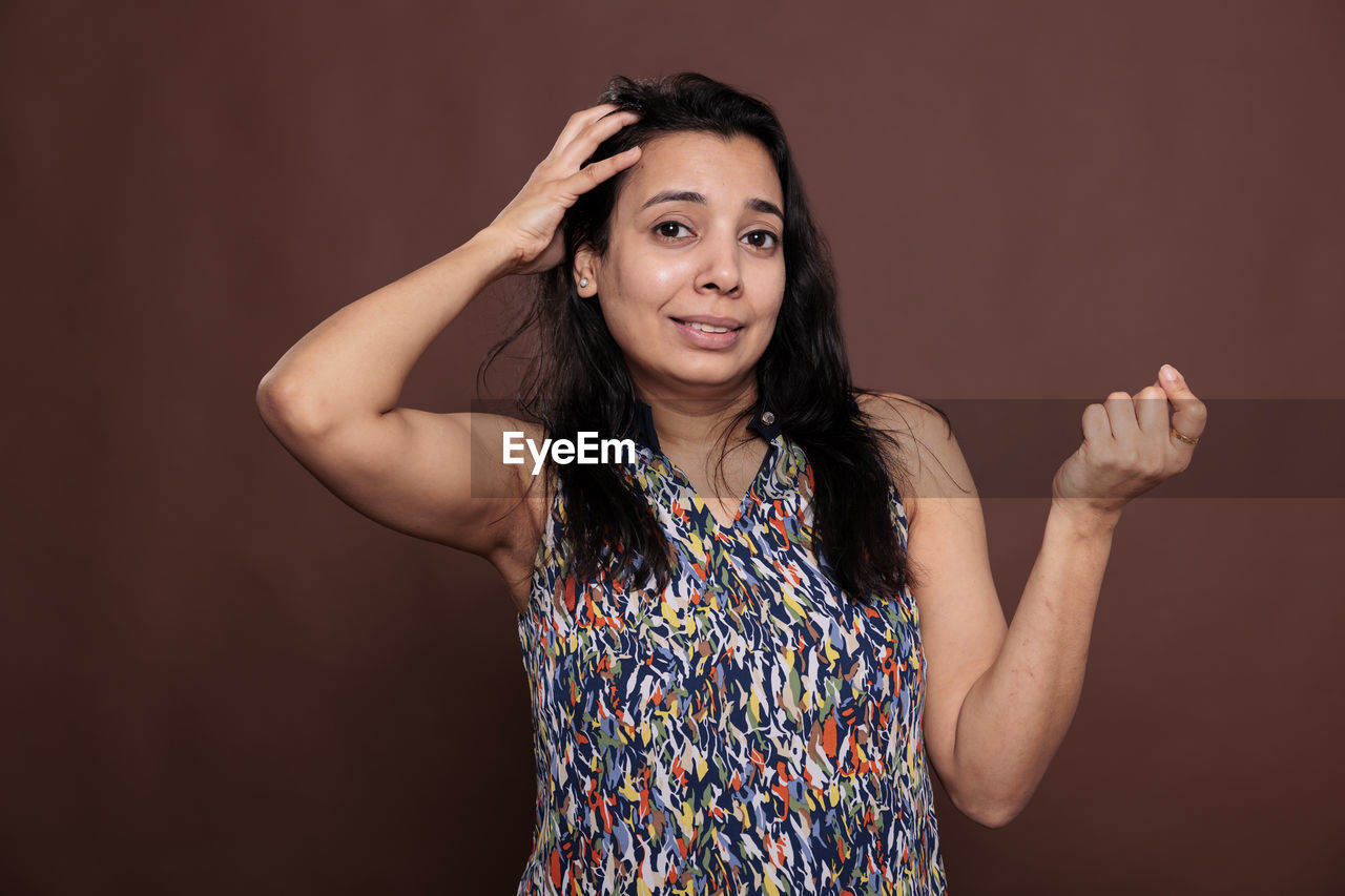 one person, portrait, studio shot, photo shoot, adult, looking at camera, women, indoors, emotion, waist up, hairstyle, front view, fashion, arm, long hair, young adult, colored background, smiling, happiness, standing, brown hair, arms raised, copy space, singing, person, black hair, limb, clothing, human limb, hand, positive emotion, cheerful, arts culture and entertainment