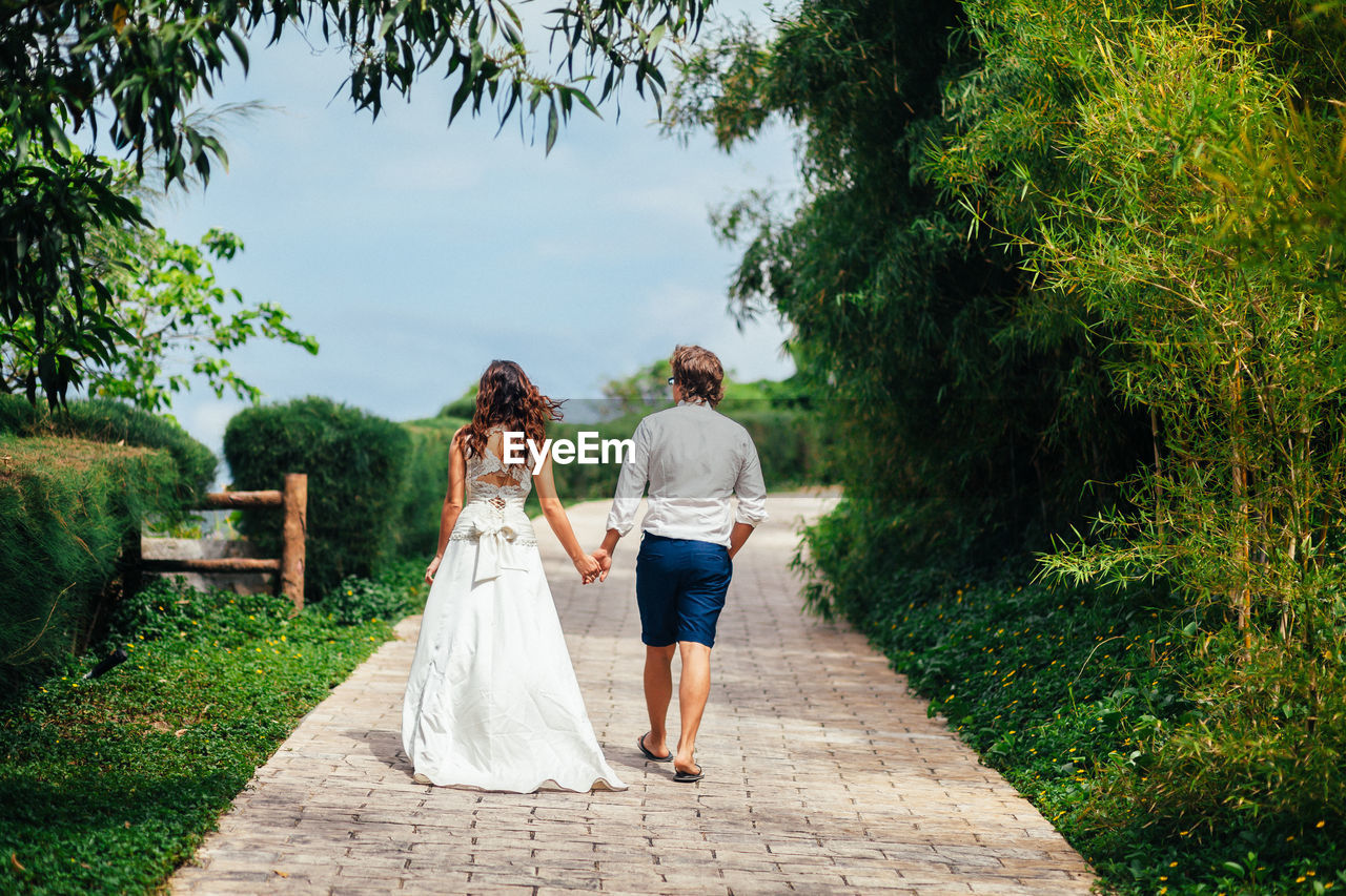 Rear view of bride and groom walking on footpath