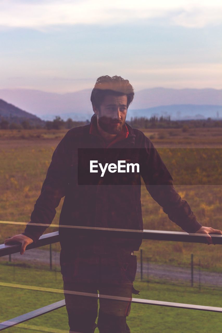 Double exposure of man standing in balcony against sky during sunset