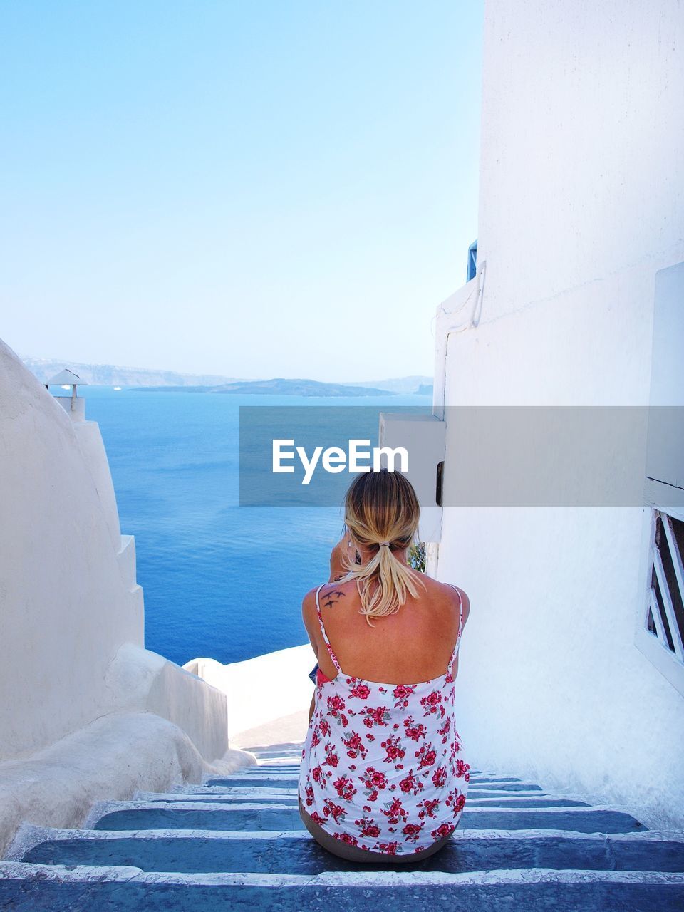 Rear view of woman sitting on steps by sea against clear sky