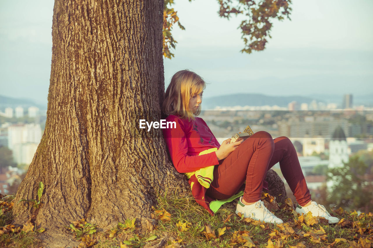 Teenage girl sitting under an autumn tree on a hill on the sunset