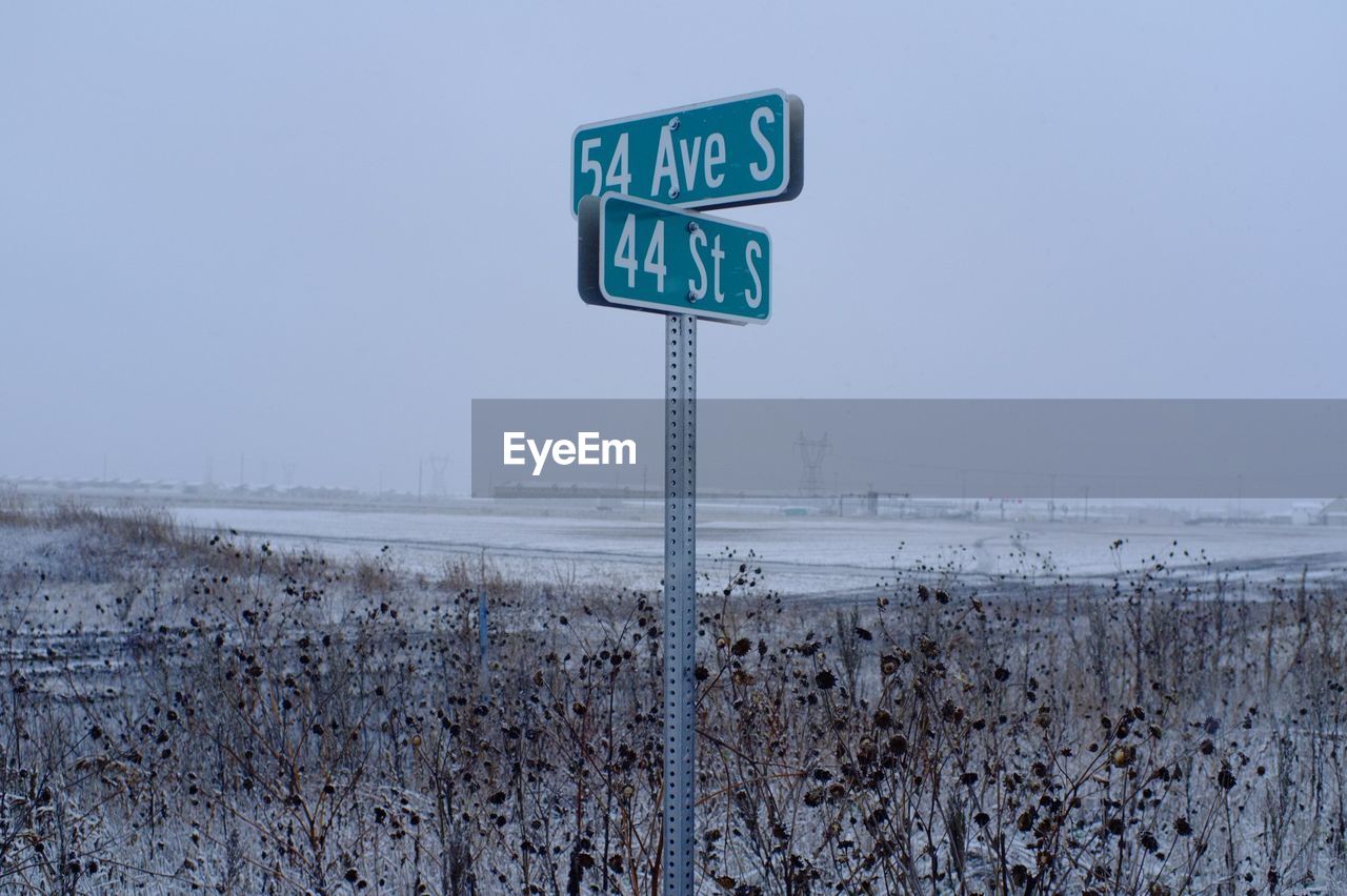 Road sign on snow covered landscape against clear sky