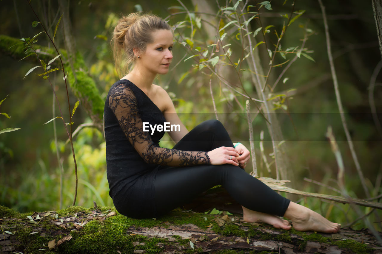 Full length of young woman sitting on tree