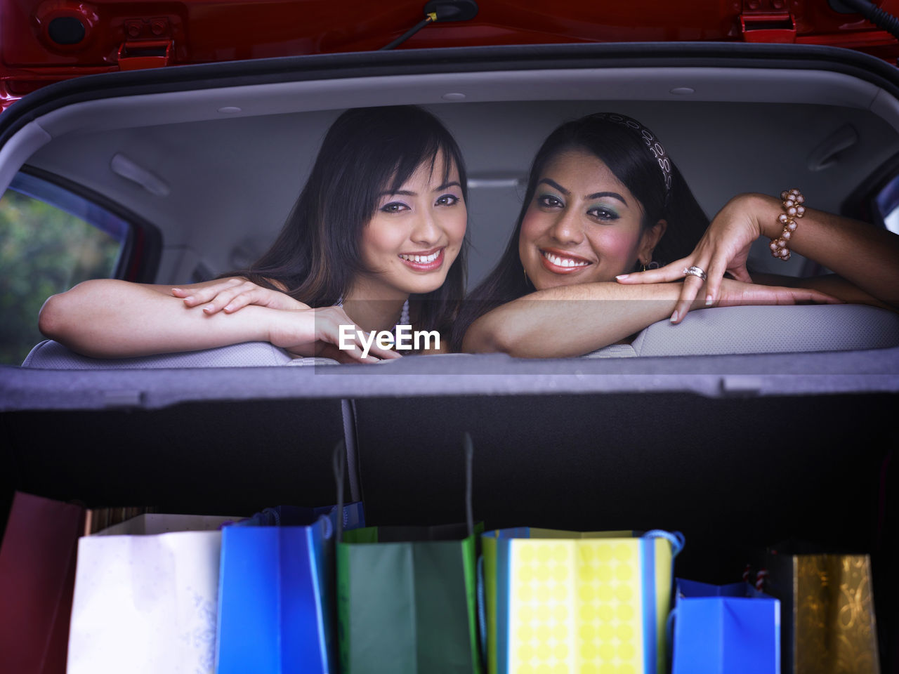 Portrait of cheerful female friends with shopping bags in car