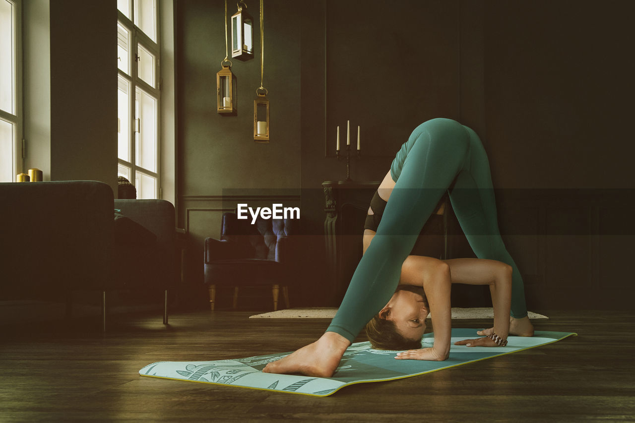 A charming girl in a sports uniform does yoga in an old room with a fireplace and candles