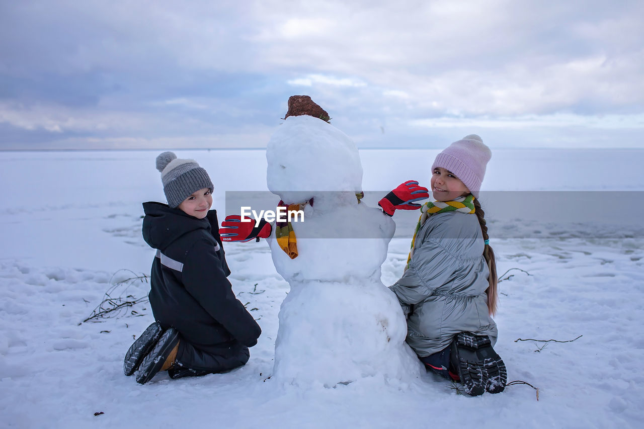 Happy boy and girl sit together with snowman. seasonal family weekend, active authentic lifestyle