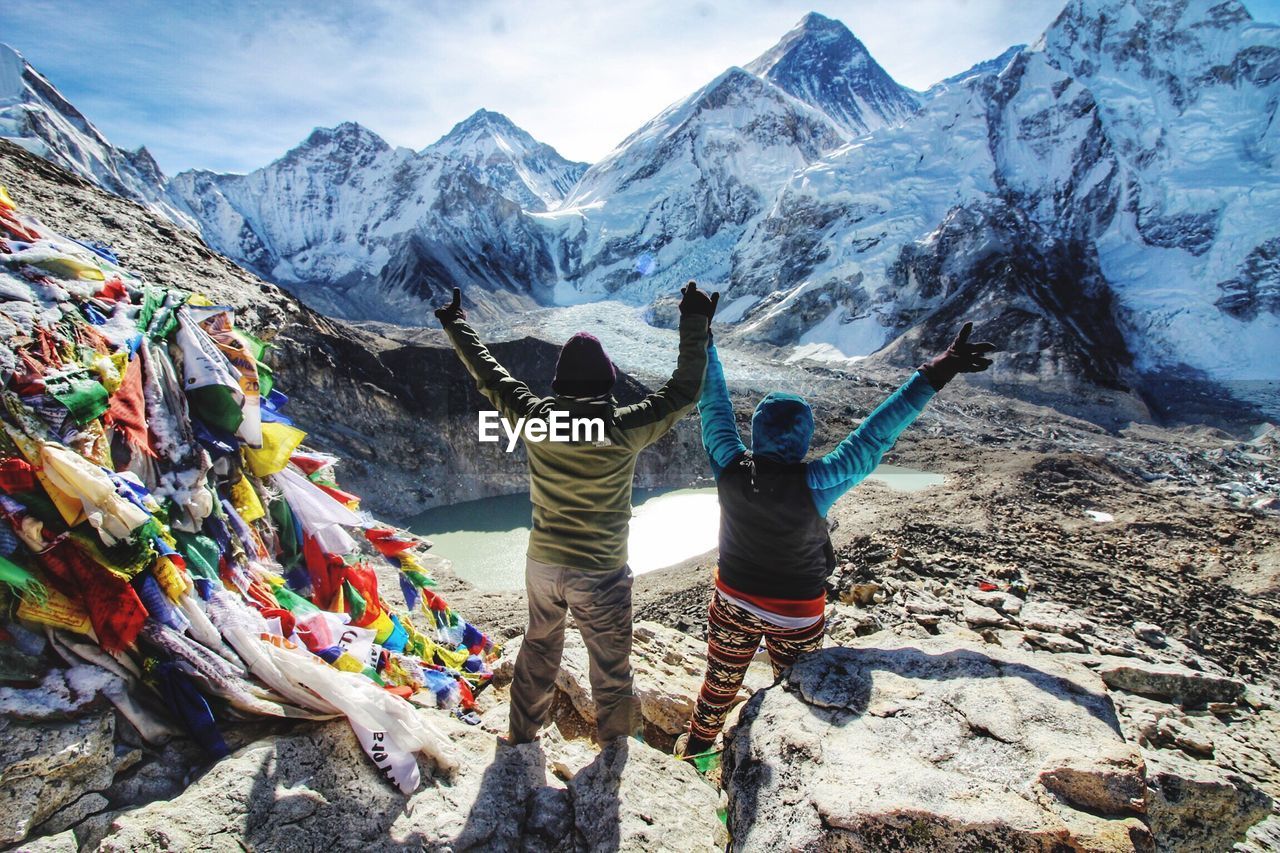 Rear view of people with arms raised standing on snow covered mountain
