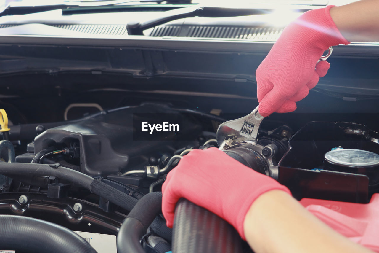 Cropped hands of mechanic holding wrench and repairing car engine