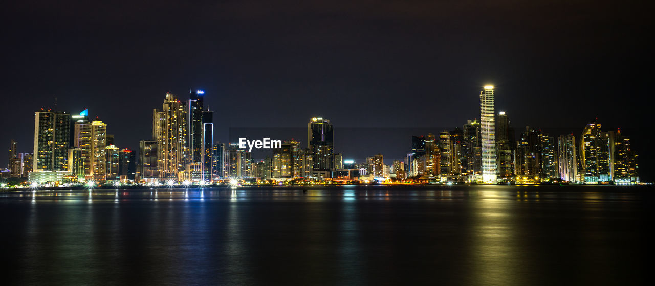 Illuminated buildings by sea against sky at night, skyline of panama