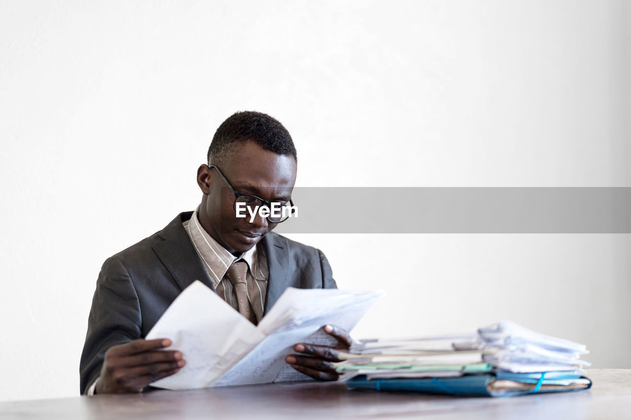 Businessman reading documents at table against white background