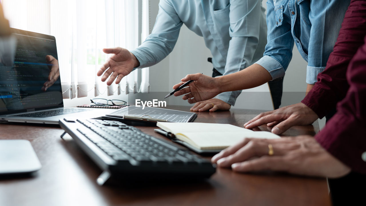 Midsection of colleagues discussing on desk in office