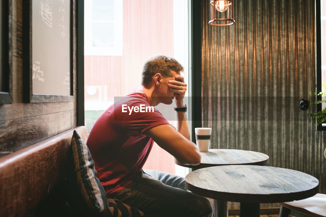 Man sat covering his face feeling stressed whilst sat in a cafe