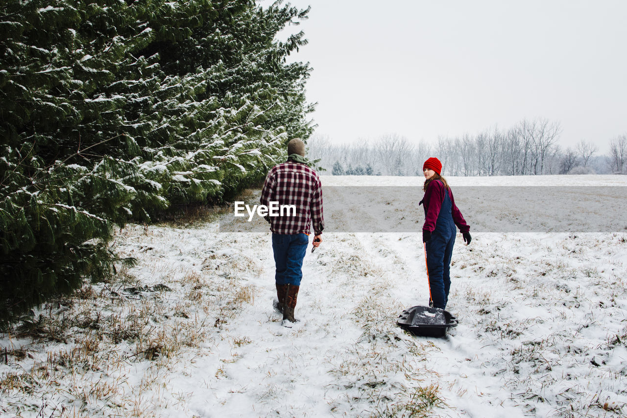 Rear view of teenage girl and boy walking on snow covered field