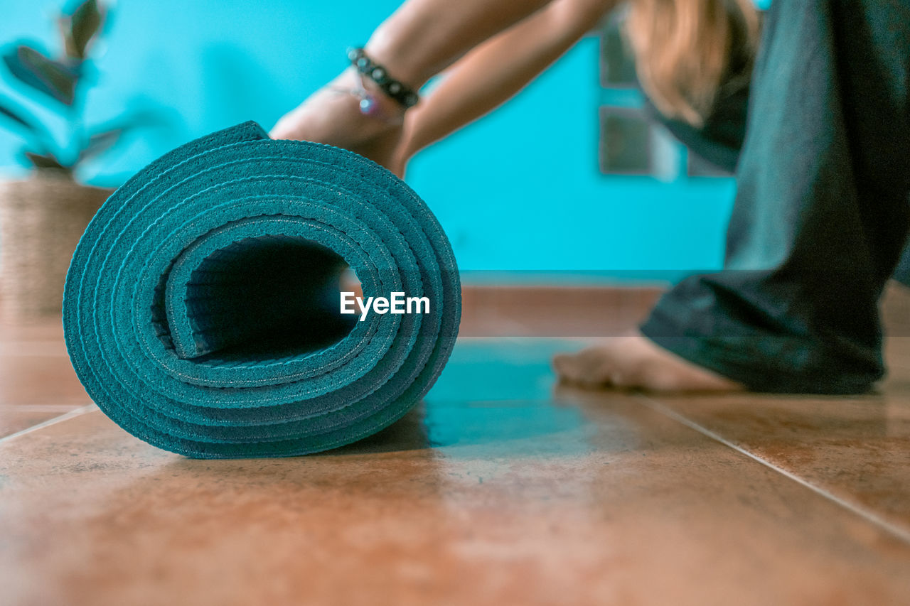 Low section of woman rolling up exercise mat at home