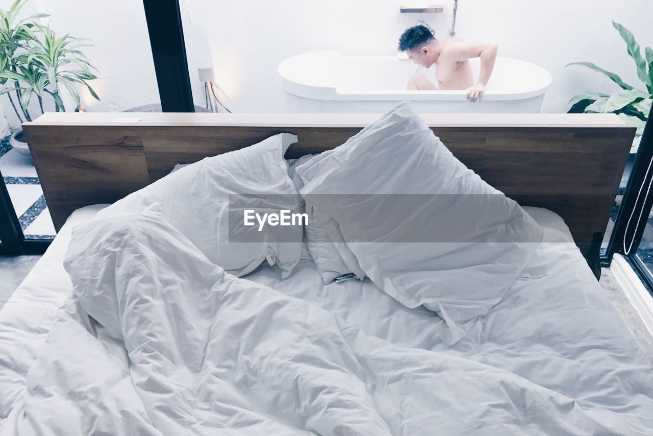 View of man in bathtub behind bed