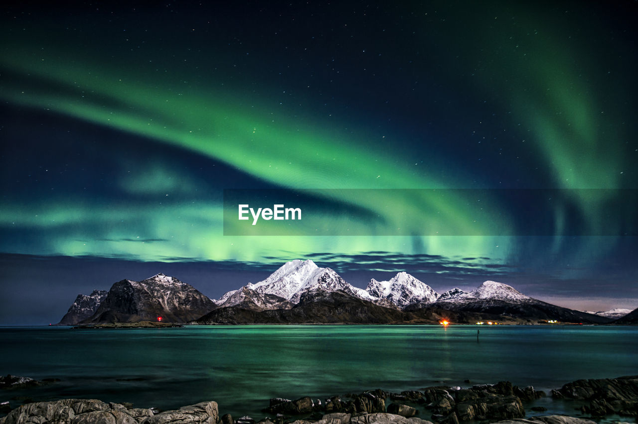 Scenic view of sea by snowcapped mountains against sky at night