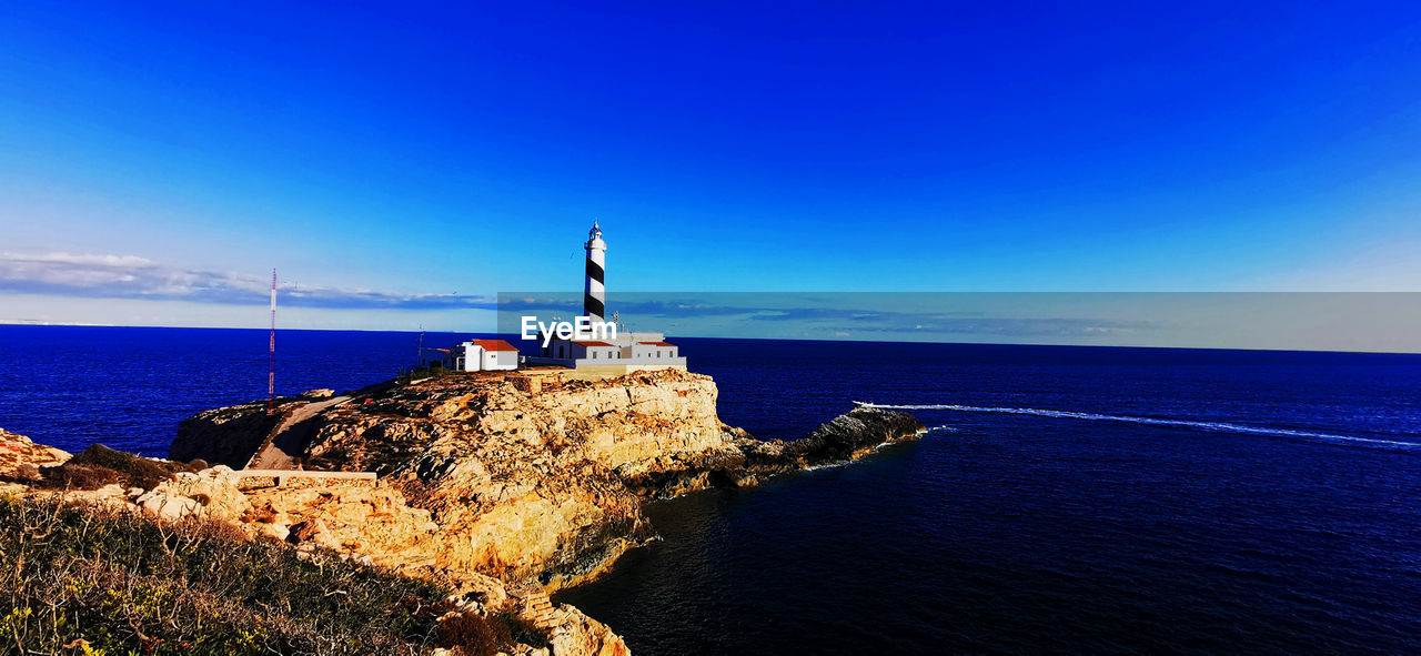 LIGHTHOUSE AMIDST ROCKS ON SEA AGAINST SKY