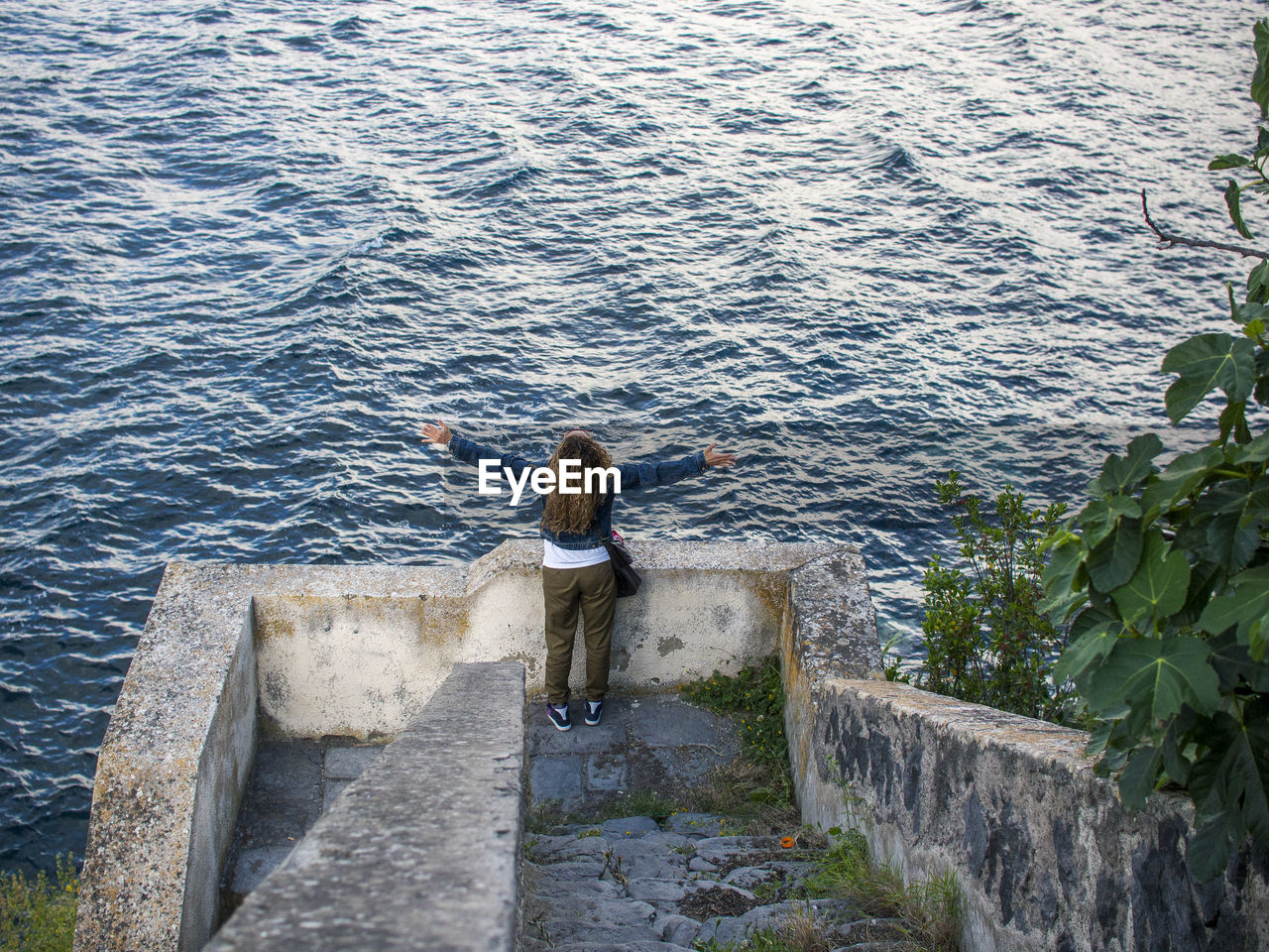 Rear view of woman standing by retaining wall against sea