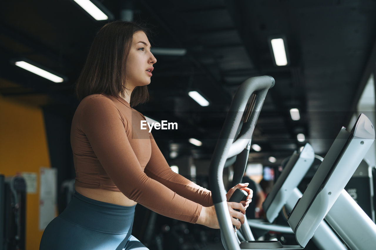 Young brunette woman training for cardio equipment at fitness gym