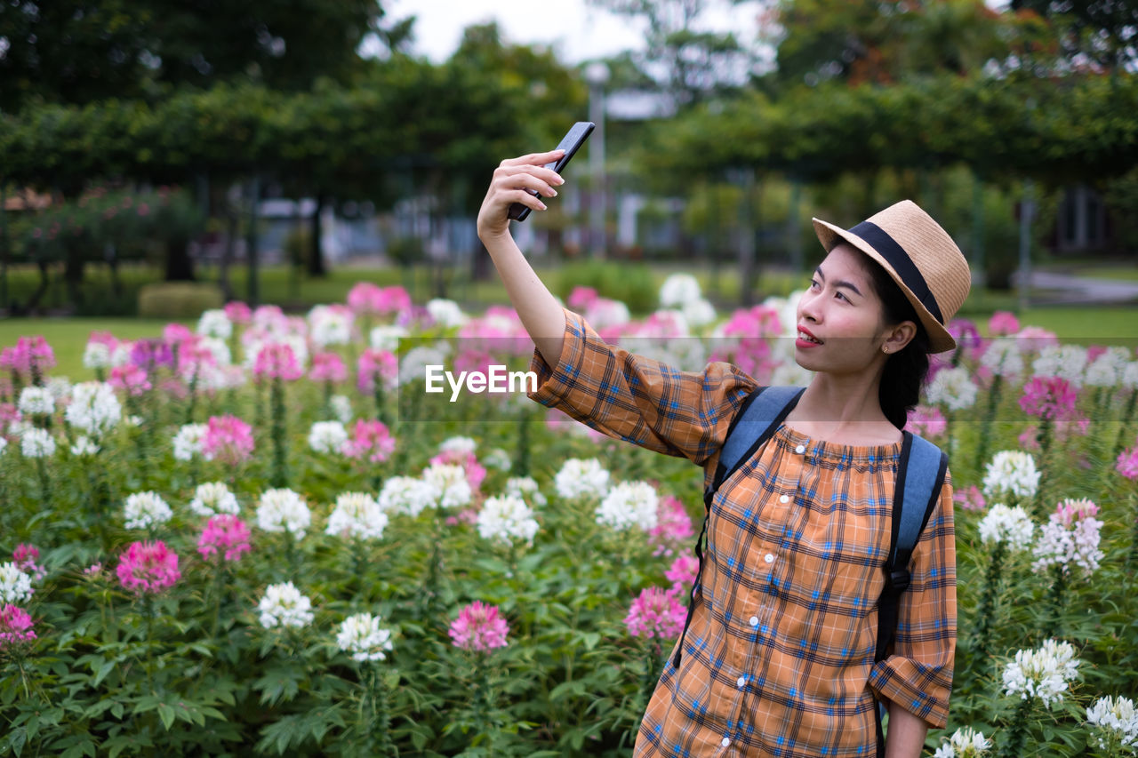 Young woman taking selfie by flowers at park