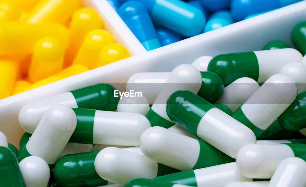 Selective focus on green-white capsule pills in plastic box on blue and yellow capsule pills. 