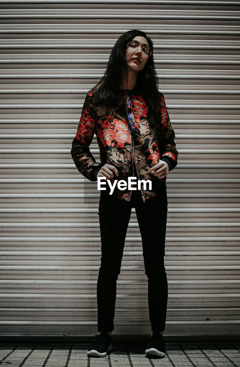 Portrait of young woman standing against shutter