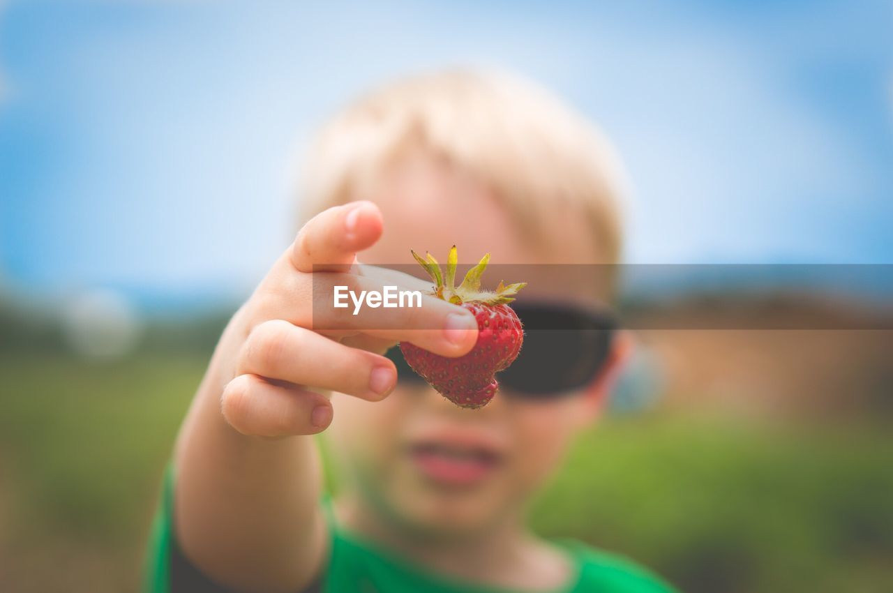 Boy wearing sunglasses while holding strawberry against sky