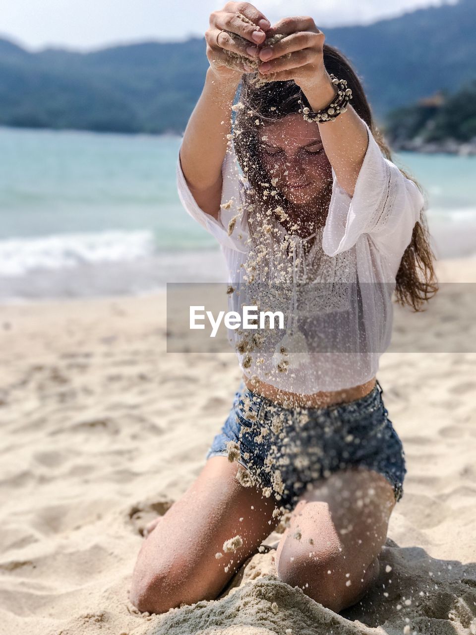 Full length of young woman playing with sand at beach