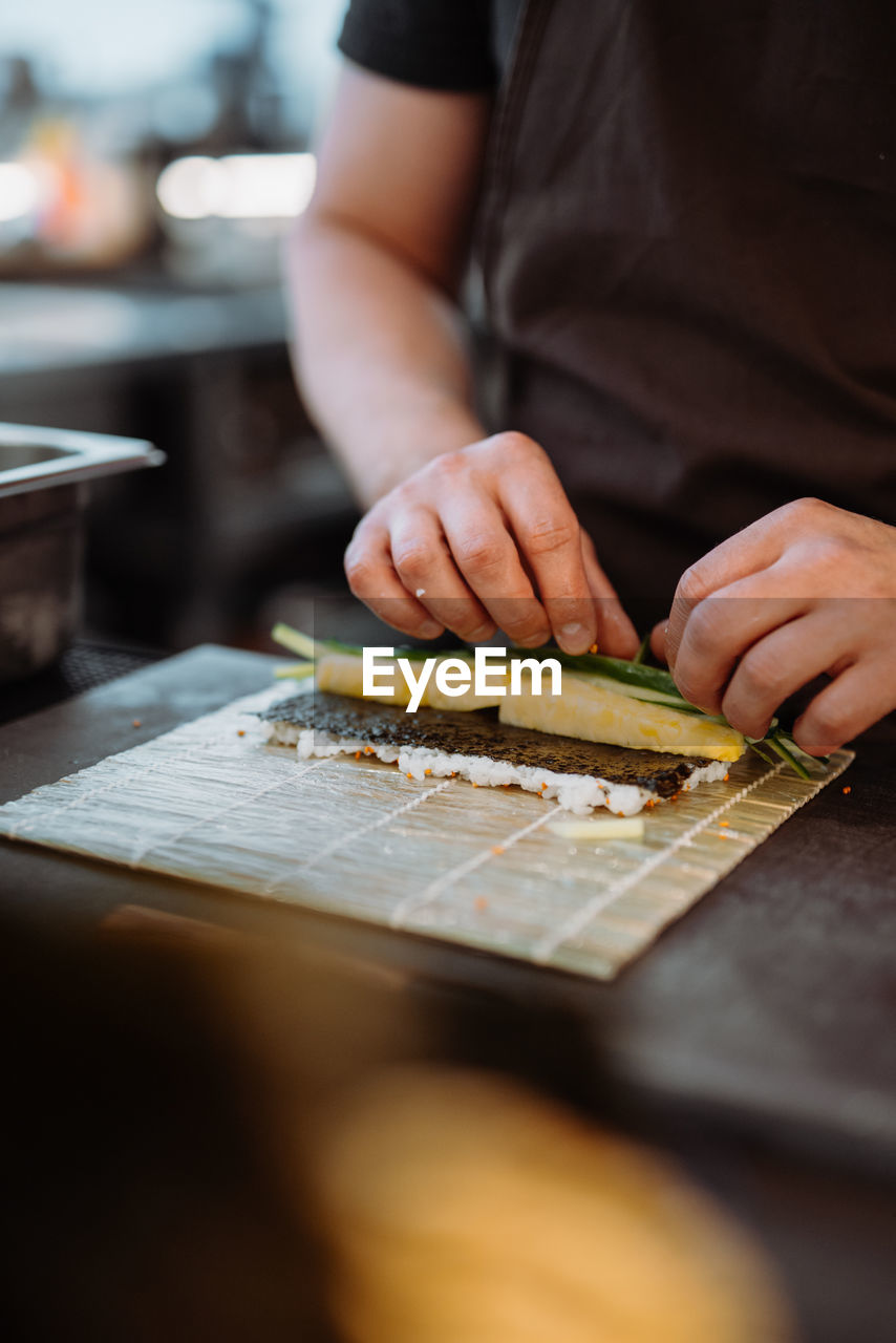 Vertical view of the hands of unknown su-chief rolling sushi and preparing sushi set in restaurant