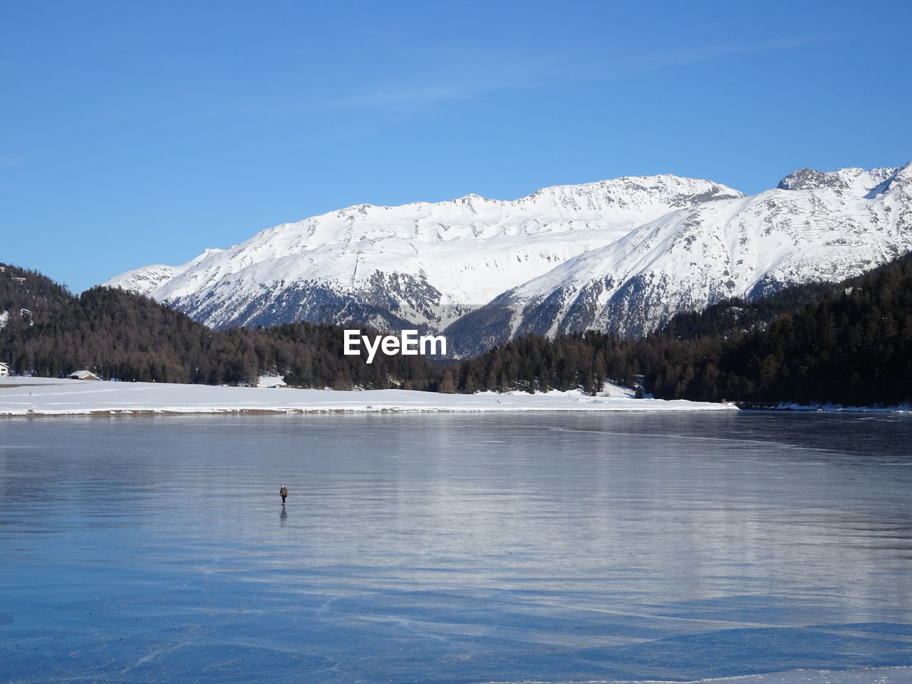 Scenic view of lake and snowcapped mountains against blue sky