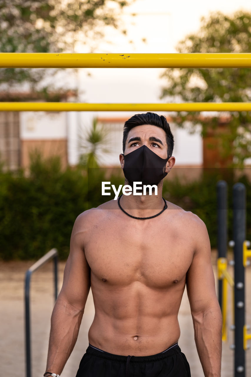 Shirtless man wearing mask exercising at park