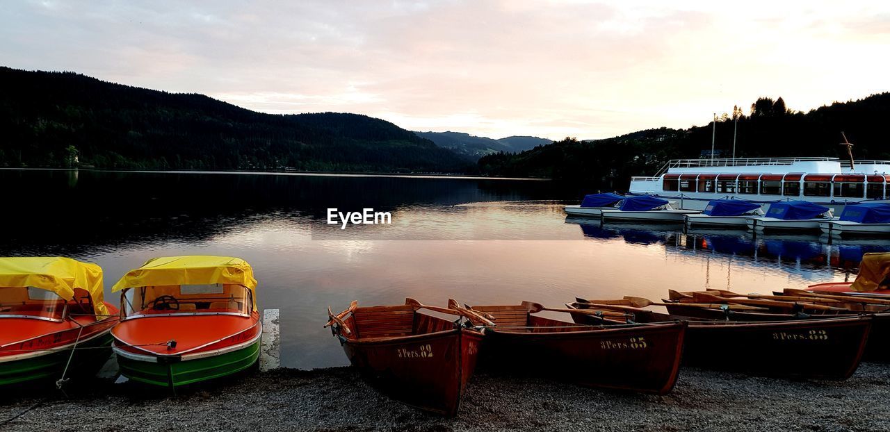 BOATS MOORED IN LAKE AGAINST SKY