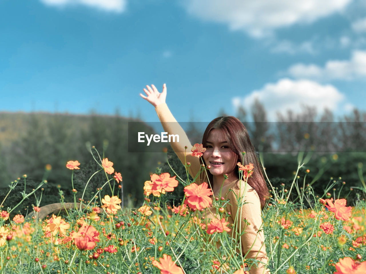 Portrait of happy woman standing amidst flowering plant 