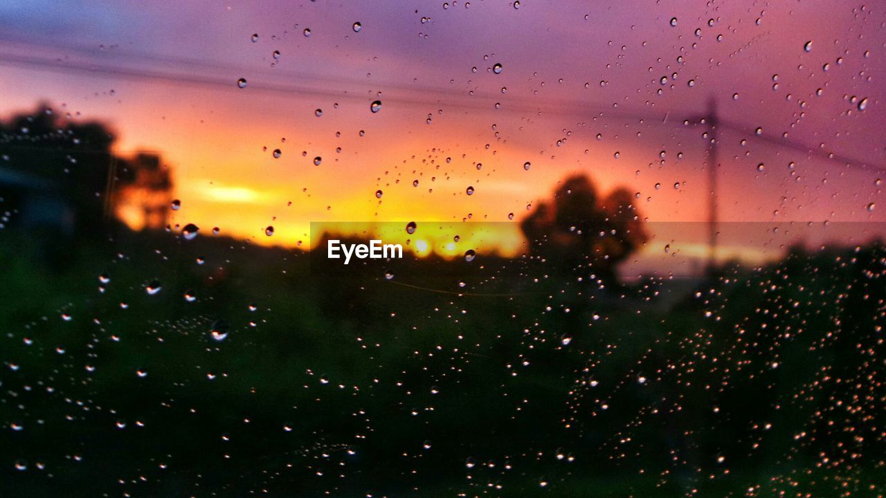 Field against orange sky seen through wet glass window during monsoon