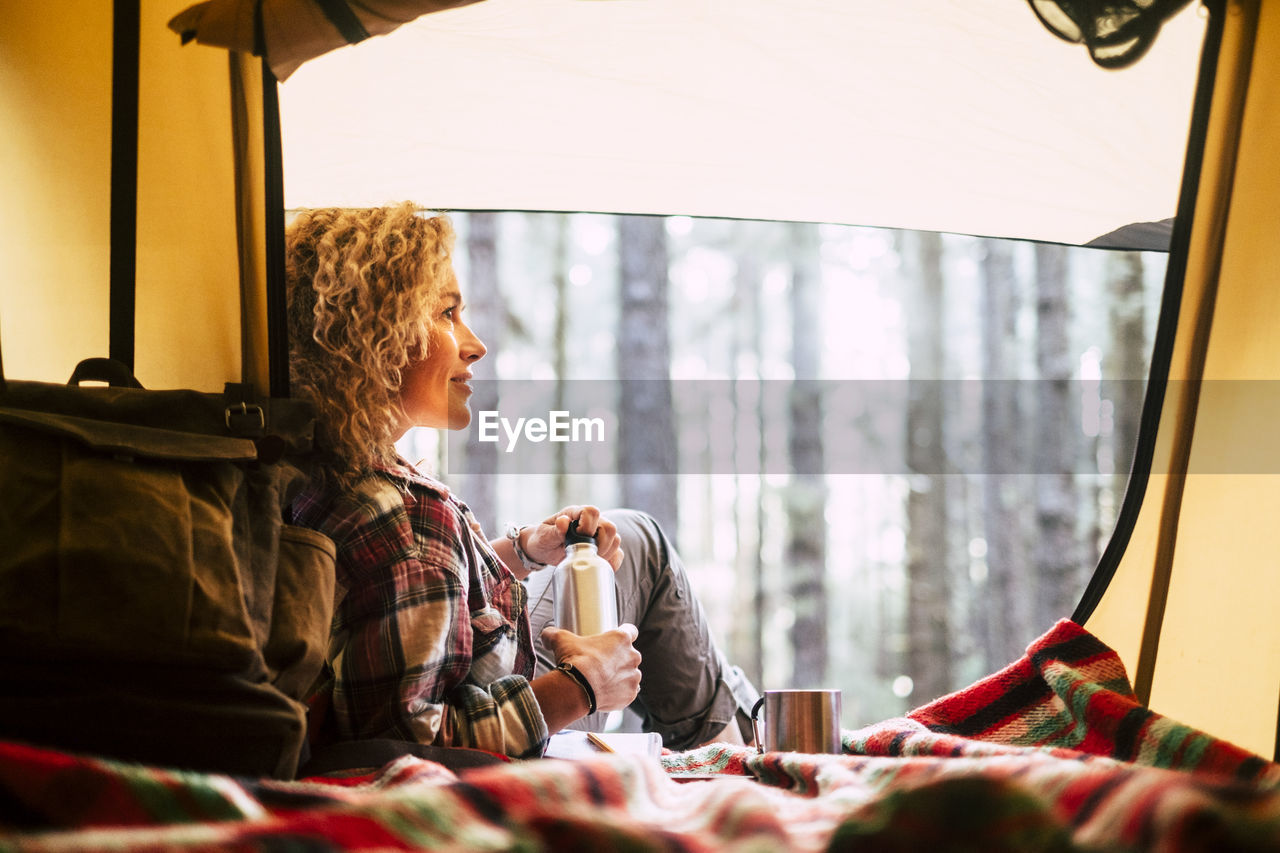 Smiling woman sitting in tent while looking away in forest