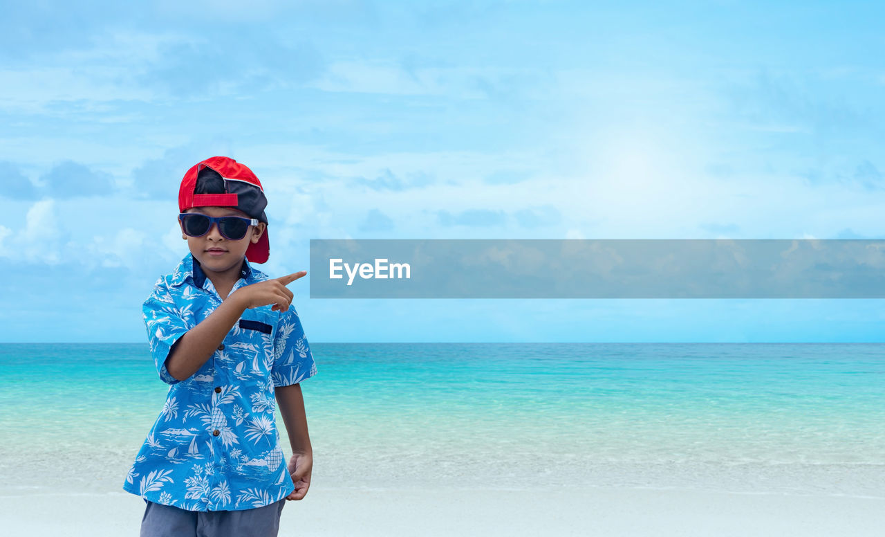 BOY STANDING IN SEA AGAINST SKY