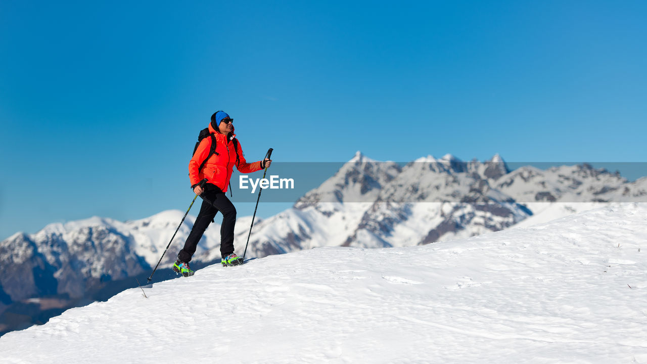 MAN SKIING ON SNOWCAPPED MOUNTAIN AGAINST CLEAR SKY